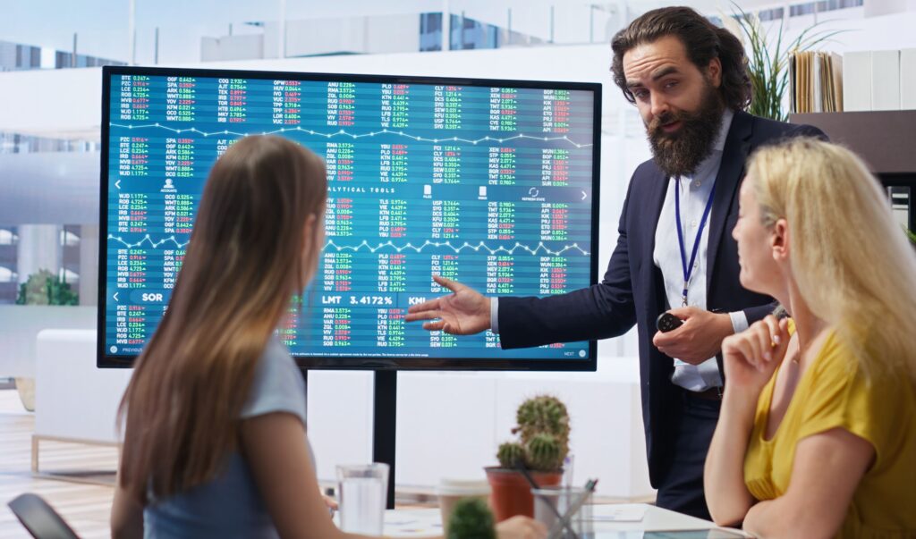 Imagen representa profesionales reunidos mirando una pantalla con datos de valoración de acciones y participaciones